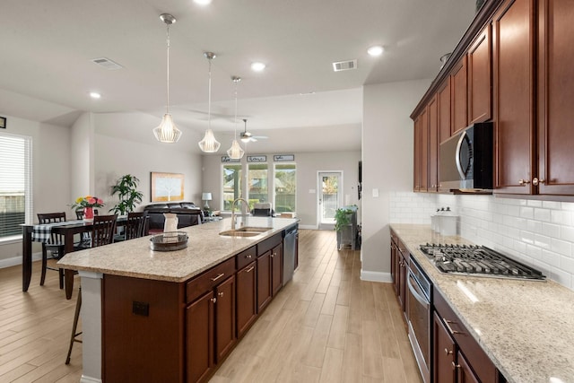 kitchen featuring pendant lighting, sink, an island with sink, stainless steel appliances, and light stone counters