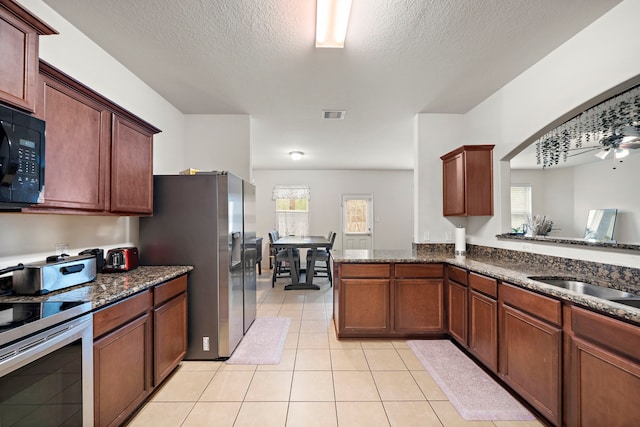 kitchen featuring light tile patterned floors, kitchen peninsula, ceiling fan, appliances with stainless steel finishes, and dark stone countertops