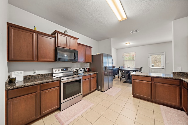 kitchen with light tile patterned floors, appliances with stainless steel finishes, dark stone countertops, and a textured ceiling