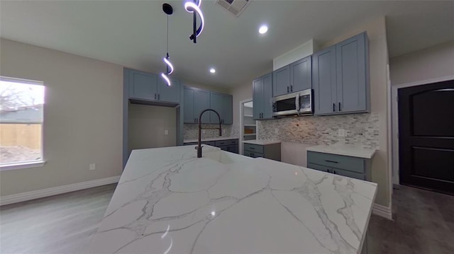 kitchen with pendant lighting, dark wood-type flooring, an island with sink, backsplash, and light stone counters