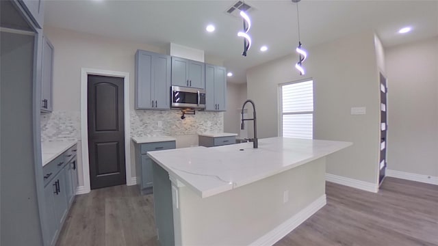 kitchen with backsplash, a center island with sink, light stone counters, and decorative light fixtures