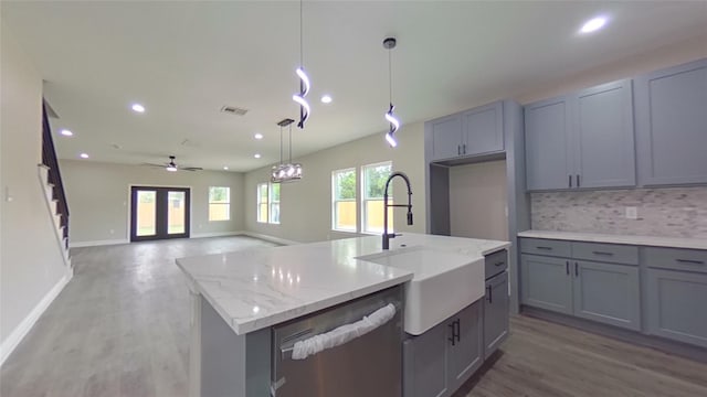 kitchen featuring a center island with sink, ceiling fan, backsplash, stainless steel dishwasher, and sink