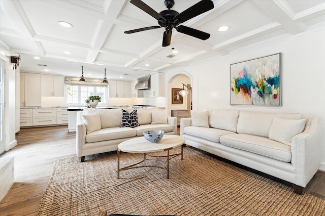 living room with coffered ceiling, ceiling fan, light wood-type flooring, ornamental molding, and beamed ceiling