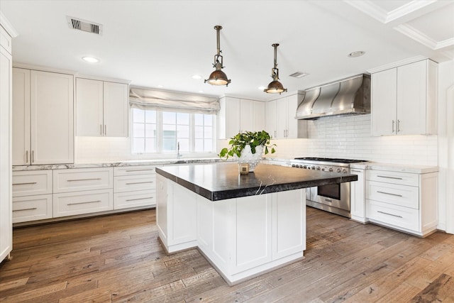 kitchen with wall chimney exhaust hood, white cabinets, and high end stove