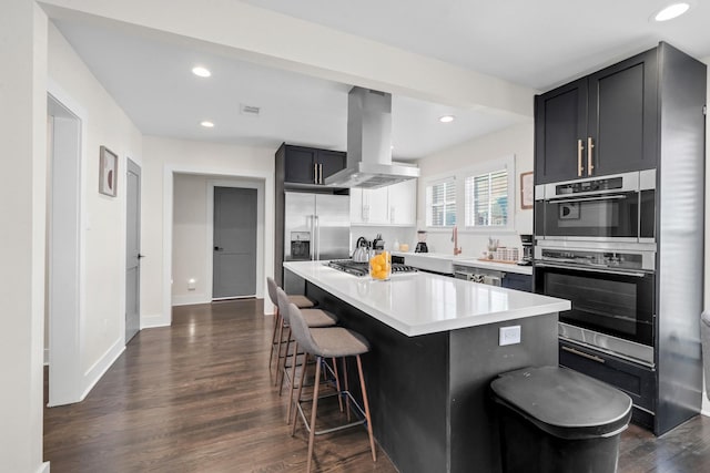 kitchen featuring dark hardwood / wood-style floors, a center island, a breakfast bar, island exhaust hood, and appliances with stainless steel finishes