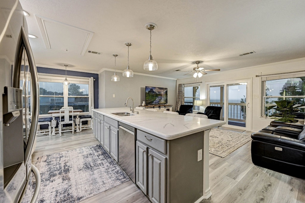 kitchen with ceiling fan, a center island with sink, light stone countertops, appliances with stainless steel finishes, and gray cabinetry