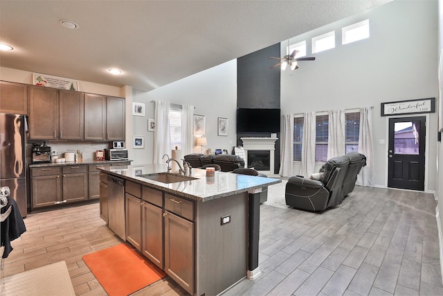 kitchen featuring a large fireplace, sink, an island with sink, stainless steel appliances, and light stone counters