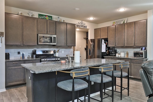 kitchen featuring appliances with stainless steel finishes, backsplash, light stone counters, a breakfast bar, and dark brown cabinets