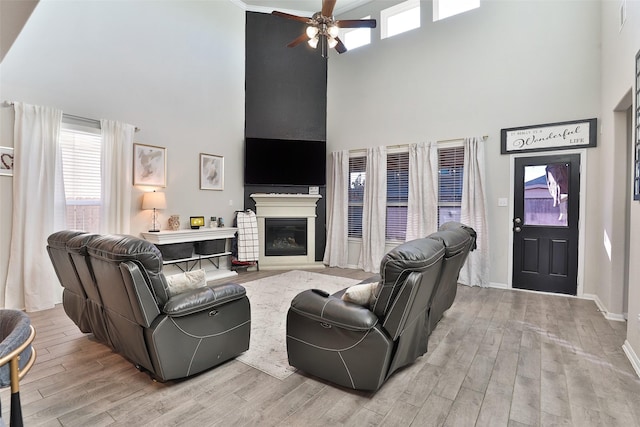 living room featuring ceiling fan, light hardwood / wood-style floors, and a towering ceiling