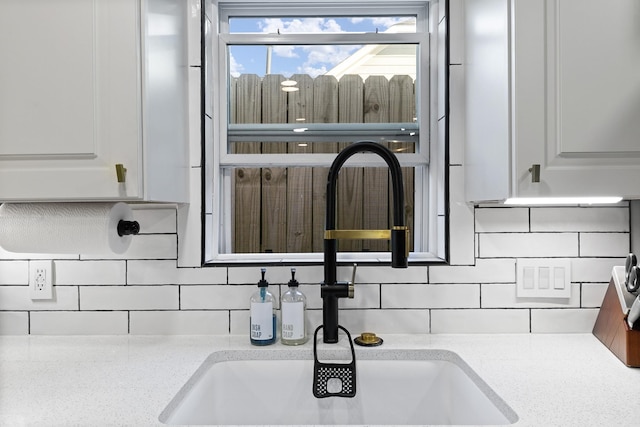 interior details featuring white cabinets, decorative backsplash, and sink