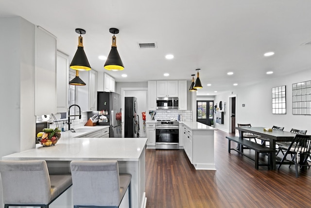 kitchen with appliances with stainless steel finishes, kitchen peninsula, tasteful backsplash, and decorative light fixtures