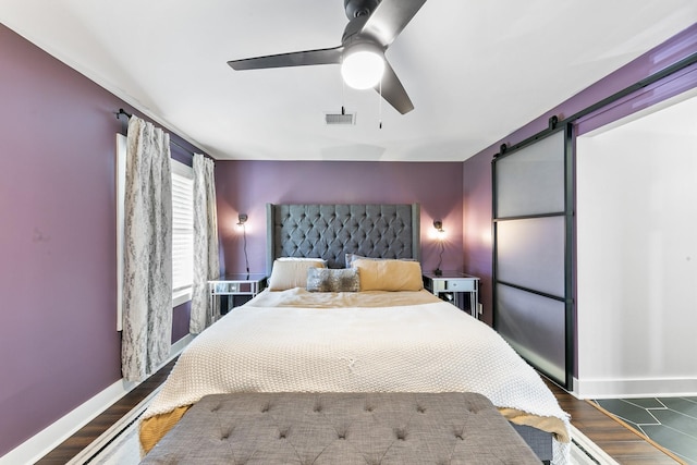 bedroom with ceiling fan, a barn door, and dark wood-type flooring