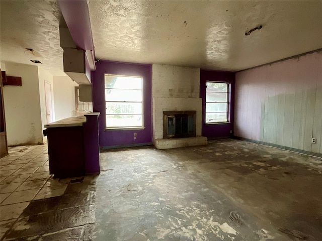 unfurnished living room featuring a large fireplace, a textured ceiling, and wooden walls