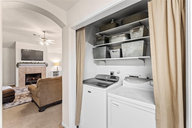 laundry area featuring ceiling fan, light colored carpet, a tile fireplace, and independent washer and dryer