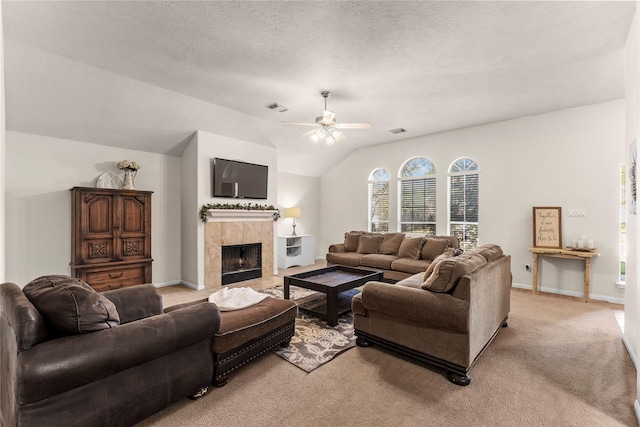 carpeted living room featuring ceiling fan, a tiled fireplace, vaulted ceiling, and a textured ceiling