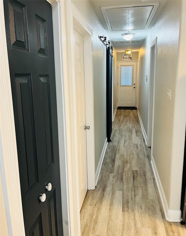 hallway featuring light wood finished floors, attic access, and baseboards