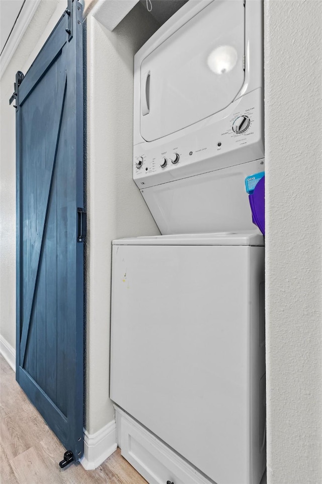 clothes washing area featuring laundry area, a barn door, baseboards, stacked washer / dryer, and light wood-style floors