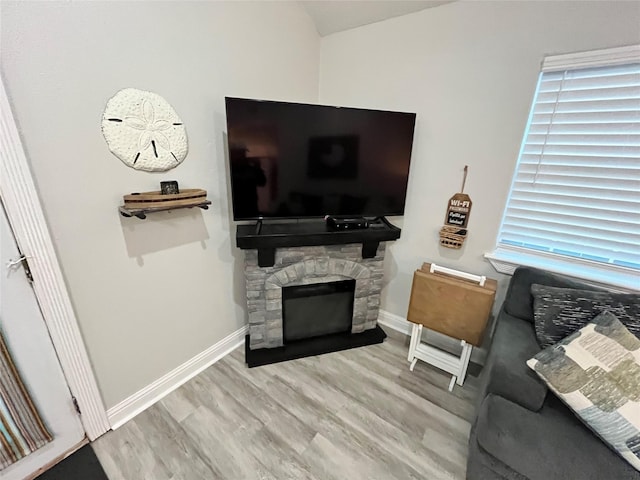 living area featuring light wood-style floors, a stone fireplace, and baseboards