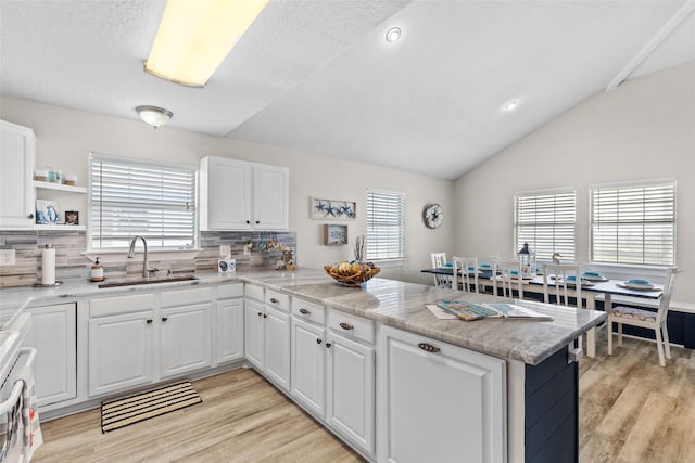 kitchen with white cabinets, lofted ceiling, a peninsula, light wood-style floors, and a sink