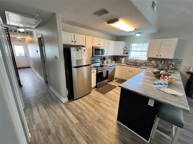 kitchen with light wood finished floors, stainless steel appliances, visible vents, a sink, and a peninsula