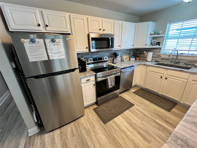 kitchen with a textured ceiling, a sink, appliances with stainless steel finishes, light wood-type flooring, and backsplash