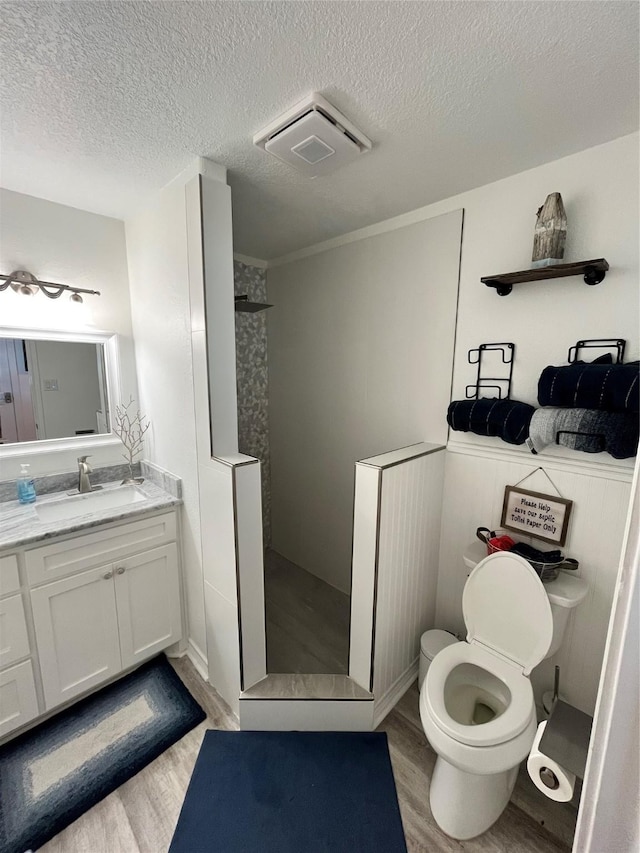 full bath featuring wood finished floors, toilet, a textured ceiling, vanity, and a walk in shower