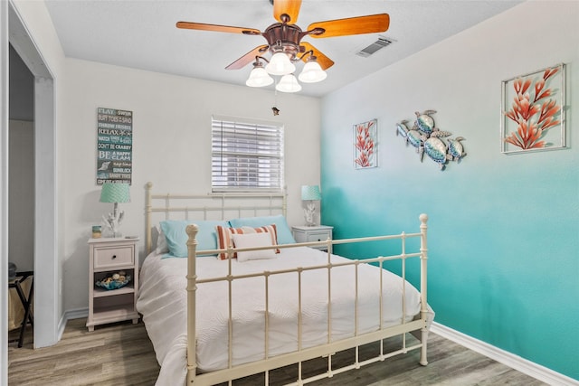 bedroom featuring a ceiling fan, visible vents, baseboards, and wood finished floors