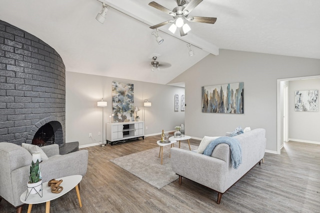 living room with ceiling fan, a fireplace, hardwood / wood-style floors, vaulted ceiling with beams, and rail lighting