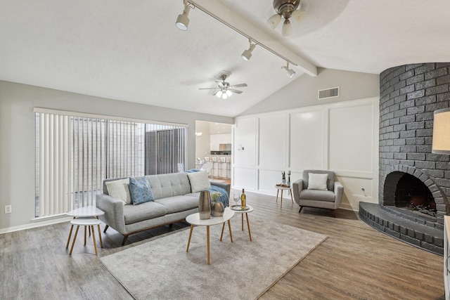 living room with a brick fireplace, wood-type flooring, lofted ceiling with beams, and ceiling fan