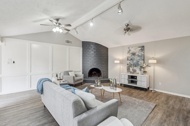 living room with hardwood / wood-style flooring, a brick fireplace, ceiling fan, lofted ceiling, and a textured ceiling