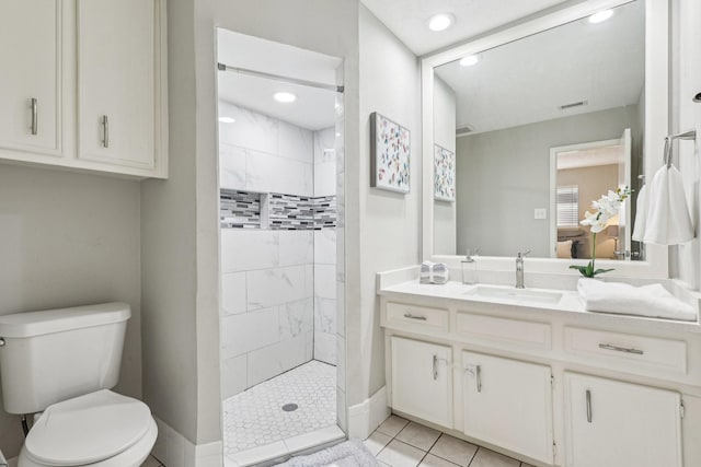 bathroom with toilet, tile patterned floors, tiled shower, and vanity