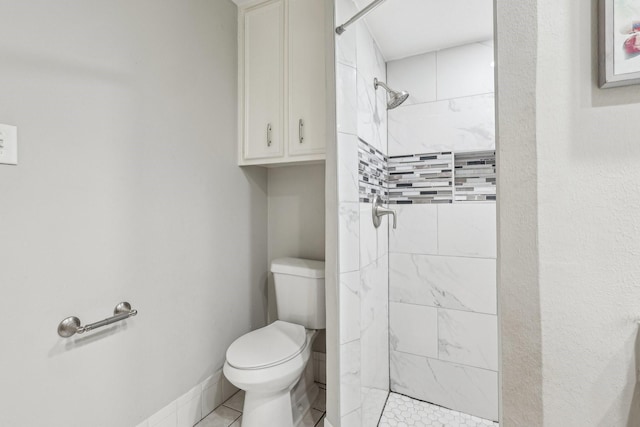 bathroom featuring toilet, tiled shower, and tile patterned flooring