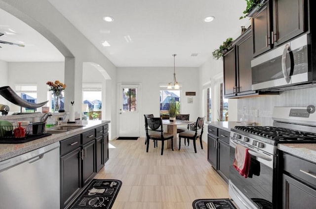 kitchen with pendant lighting, sink, dark brown cabinetry, stainless steel appliances, and ceiling fan with notable chandelier