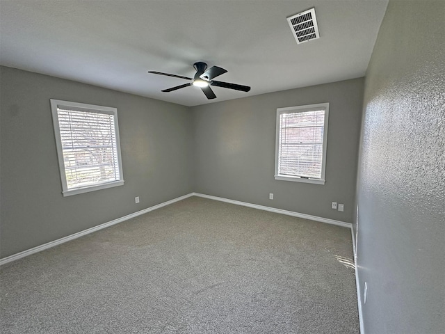 empty room featuring ceiling fan, a wealth of natural light, and carpet flooring