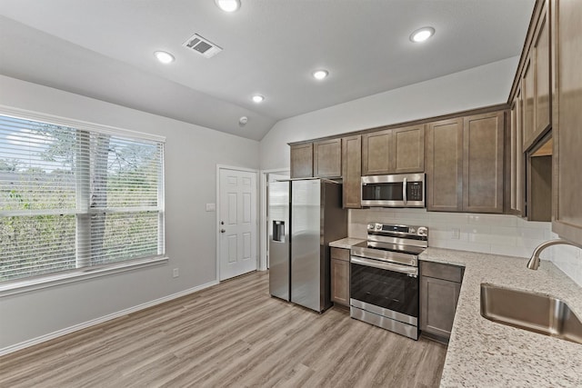 kitchen featuring appliances with stainless steel finishes, tasteful backsplash, lofted ceiling, light stone counters, and sink