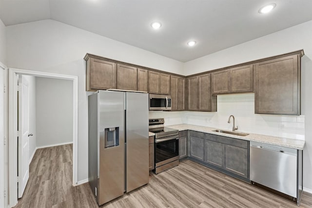 kitchen with appliances with stainless steel finishes, sink, vaulted ceiling, light stone counters, and dark brown cabinets