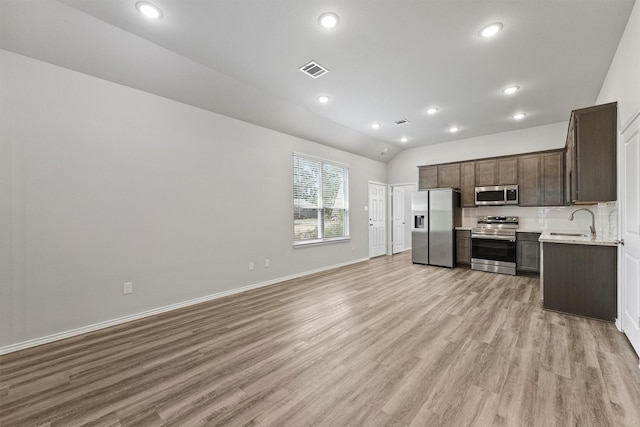 kitchen featuring lofted ceiling, stainless steel appliances, tasteful backsplash, sink, and light wood-type flooring