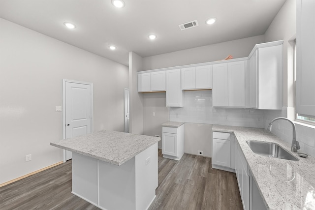 kitchen featuring dark hardwood / wood-style floors, sink, white cabinets, light stone counters, and a center island