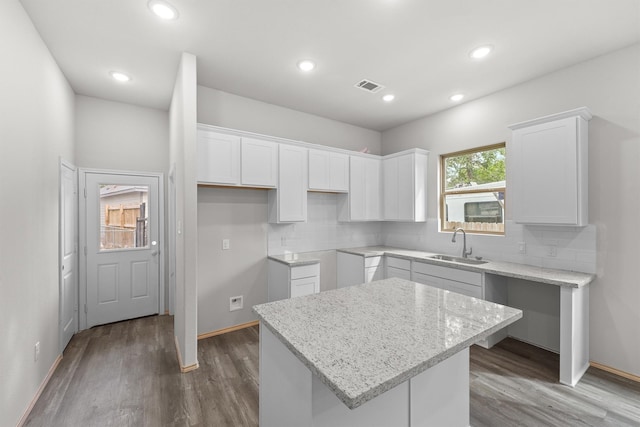 kitchen with a kitchen island, decorative backsplash, sink, light stone countertops, and white cabinets