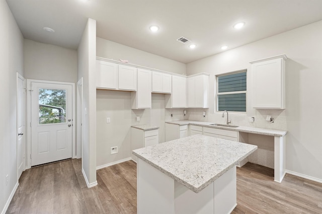 kitchen with a center island, sink, light hardwood / wood-style flooring, white cabinets, and light stone counters