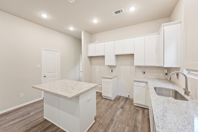 kitchen featuring white cabinetry, sink, wood-type flooring, light stone counters, and a center island