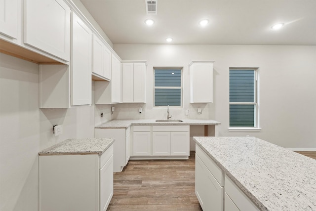 kitchen featuring light hardwood / wood-style floors, sink, white cabinetry, and light stone countertops