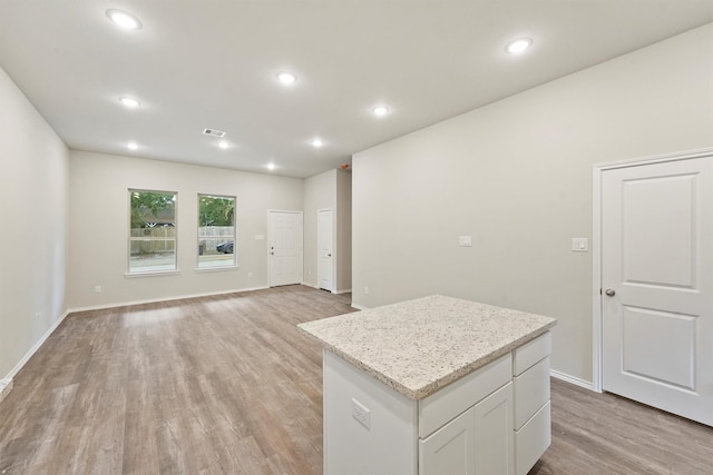 kitchen with light hardwood / wood-style floors, light stone counters, white cabinetry, and a center island