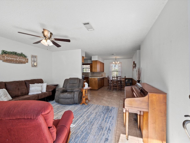 tiled living room with ceiling fan with notable chandelier and a textured ceiling