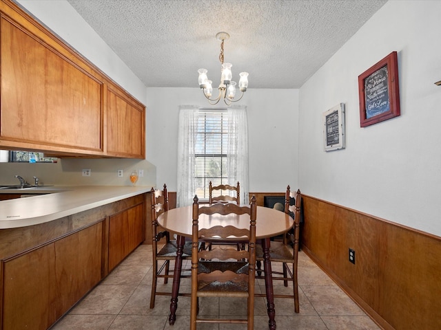 tiled dining space featuring an inviting chandelier, wooden walls, sink, and a textured ceiling