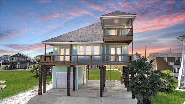 raised beach house with french doors, a balcony, a yard, and a garage