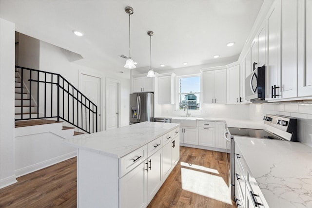 kitchen with white cabinetry, light stone counters, a center island, pendant lighting, and stainless steel appliances