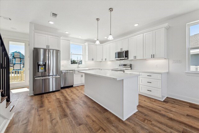 kitchen featuring pendant lighting, backsplash, stainless steel appliances, white cabinets, and a kitchen island