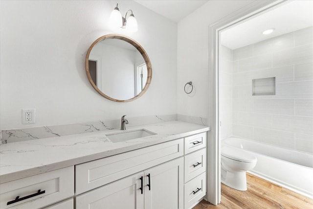 full bathroom featuring wood-type flooring, tiled shower / bath, vanity, and toilet