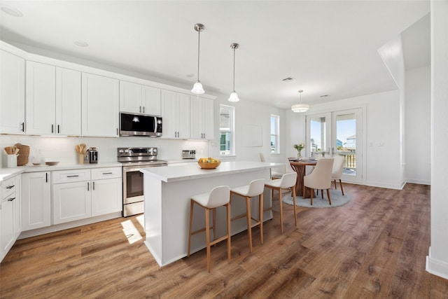 kitchen featuring decorative light fixtures, white cabinetry, a breakfast bar area, a center island, and stainless steel appliances